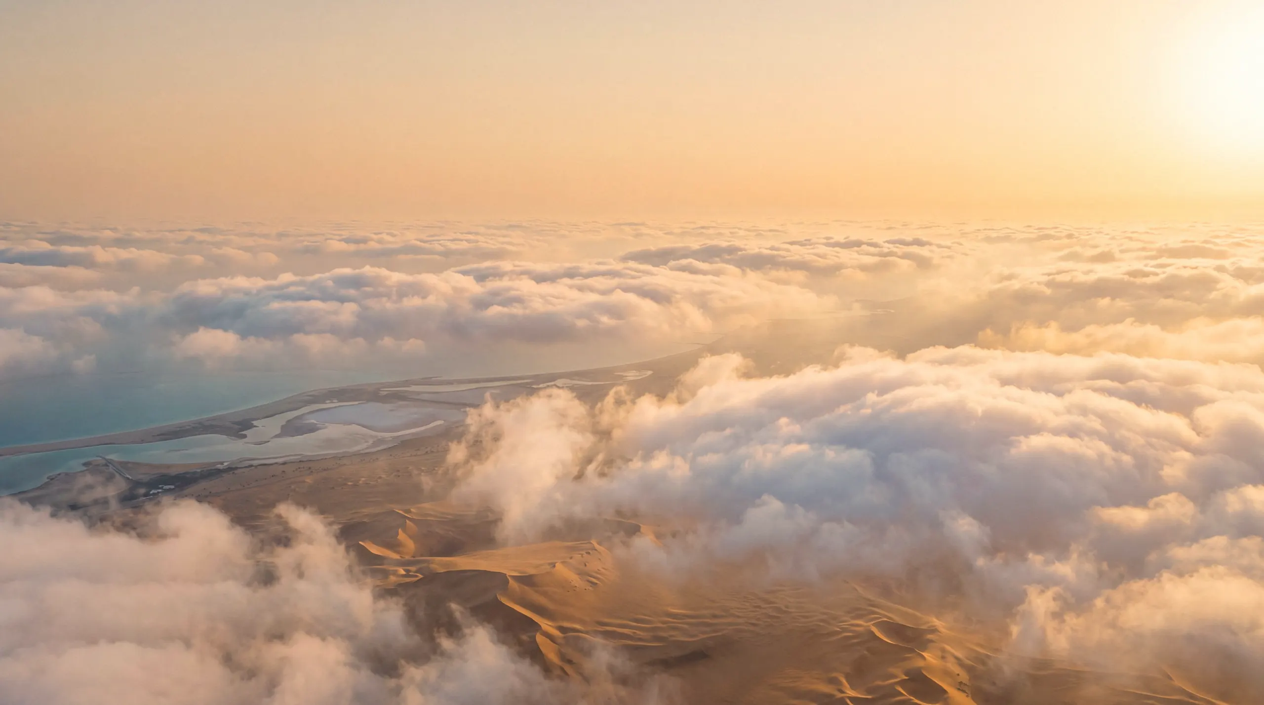 Flying through low cumulus clouds at golden hour, with desert dunes and the coastline visible far below