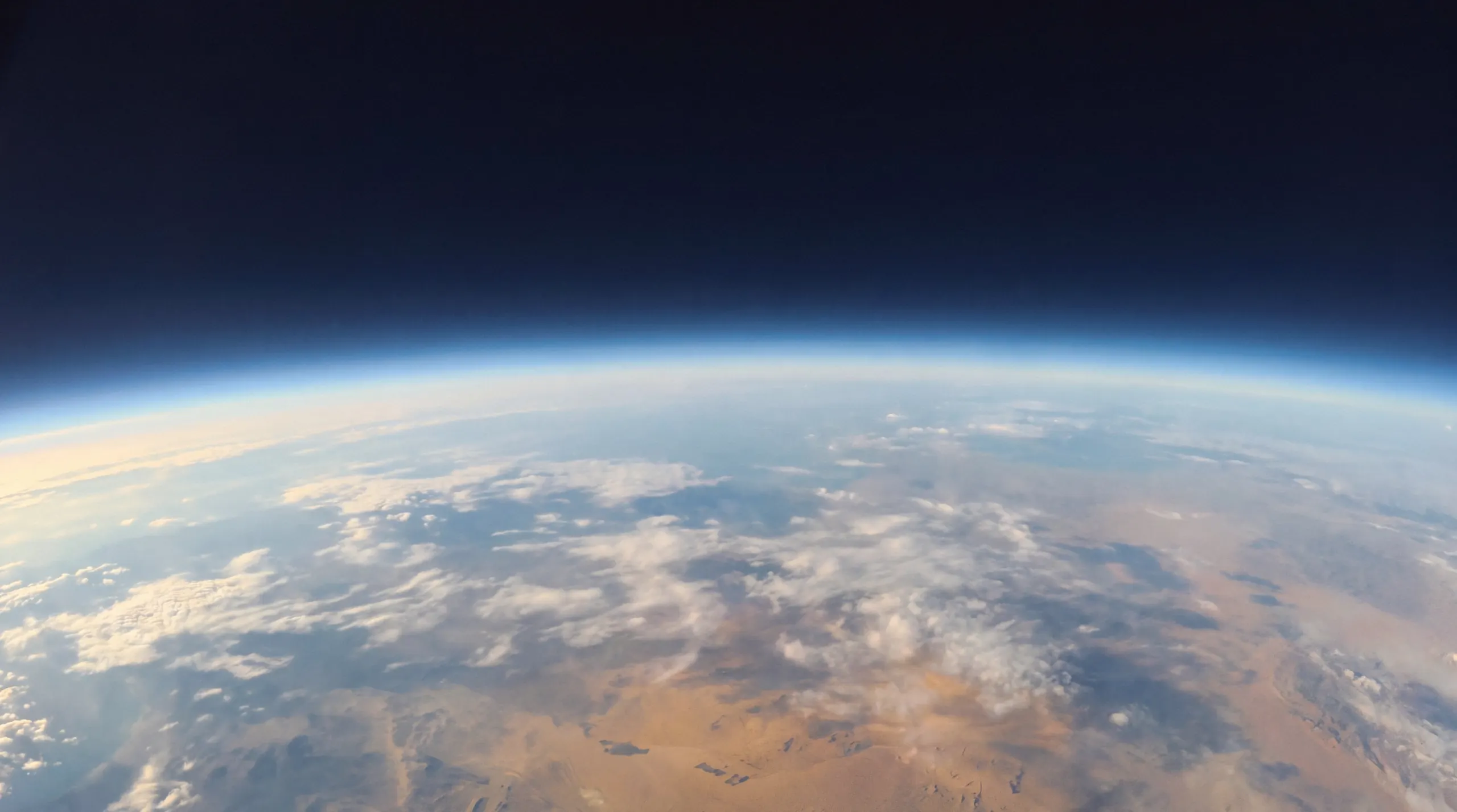 The curved horizon of the Earth seen from the stratosphere, with a thin blue band of atmosphere and a near-black sky